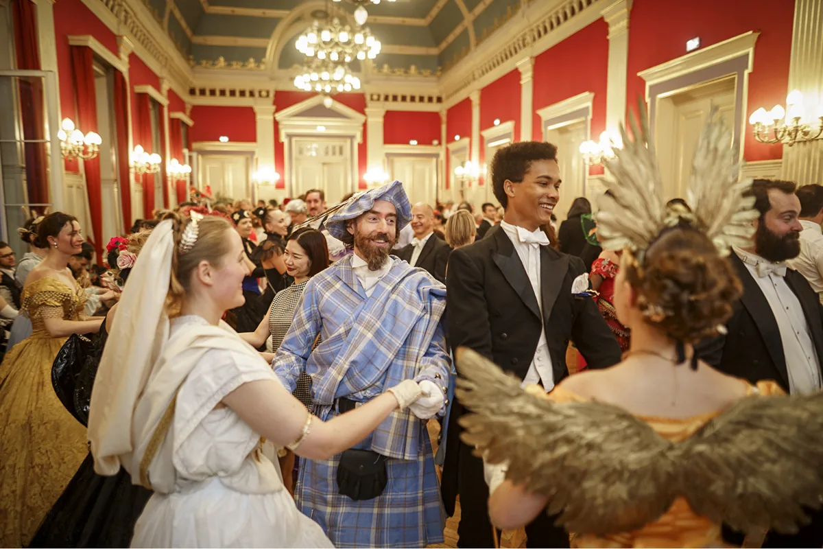 Danseurs en costumes historiques partageant un bal dans un salon aux murs rouges