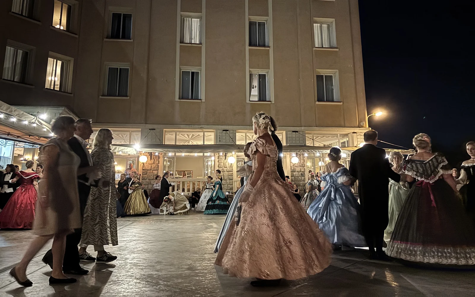 Couples en costumes du Second Empire sur la piste du Grand Bal, devant la façade éclairée du château Piccioni