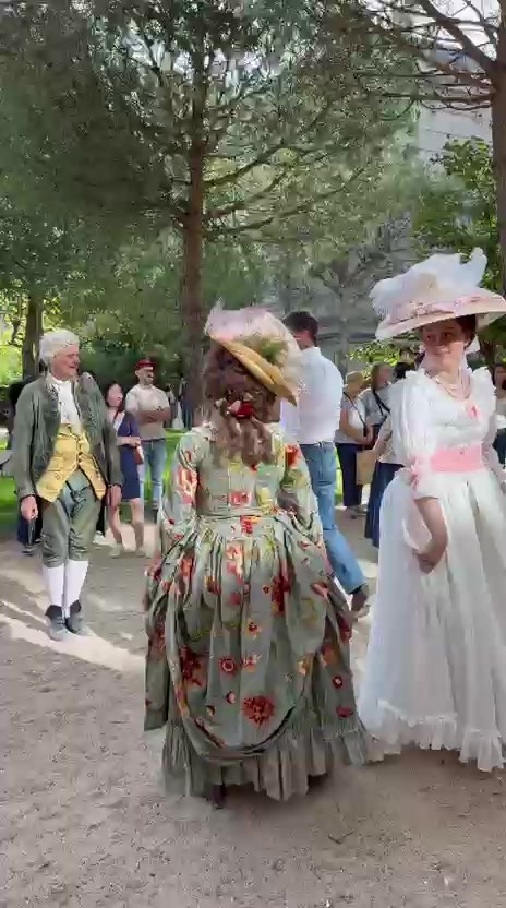 Danseuses en robe fleurie et en robe blanche à ruban rose sous les arbres des jardins de l’Hôtel de Rohan