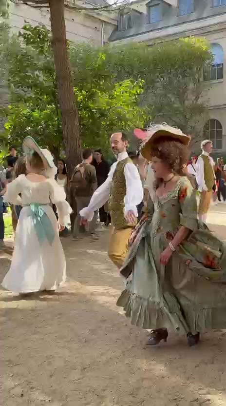 Danseuse en robe fleurie et danseur en habit doré en mouvement dans les jardins de l’Hôtel de Rohan