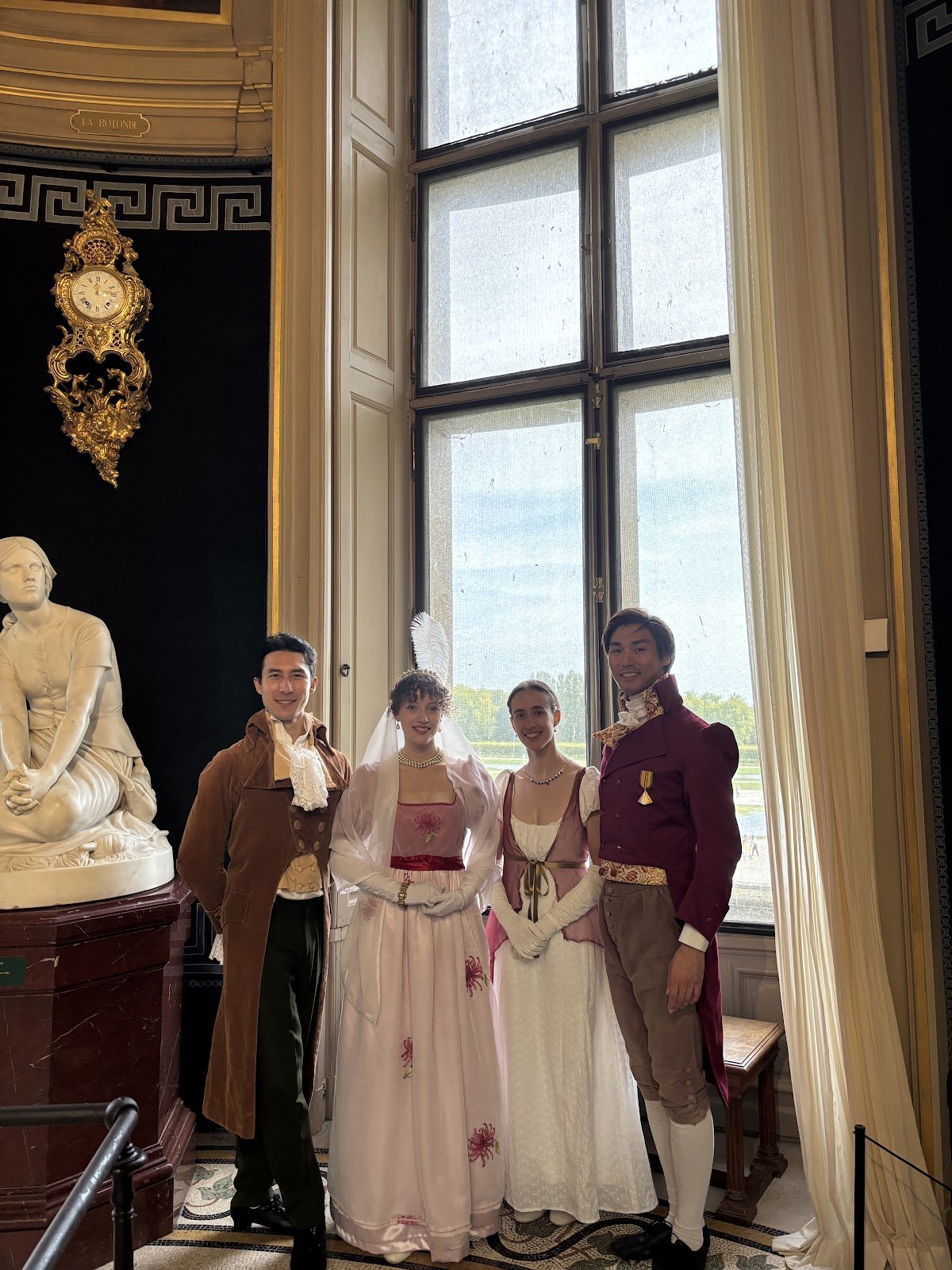 Quatre participants en costumes Premier Empire posant près d’une fenêtre du château de Chantilly