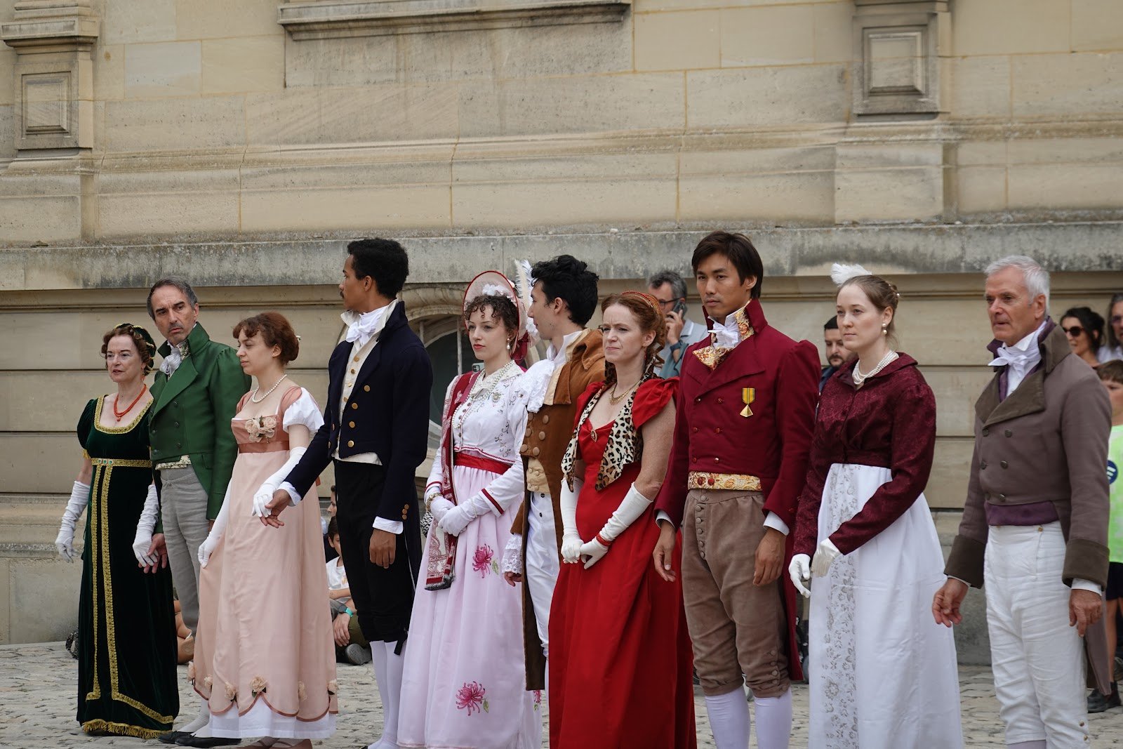 Danseuses et danseurs alignés en costumes Premier Empire devant la façade du château