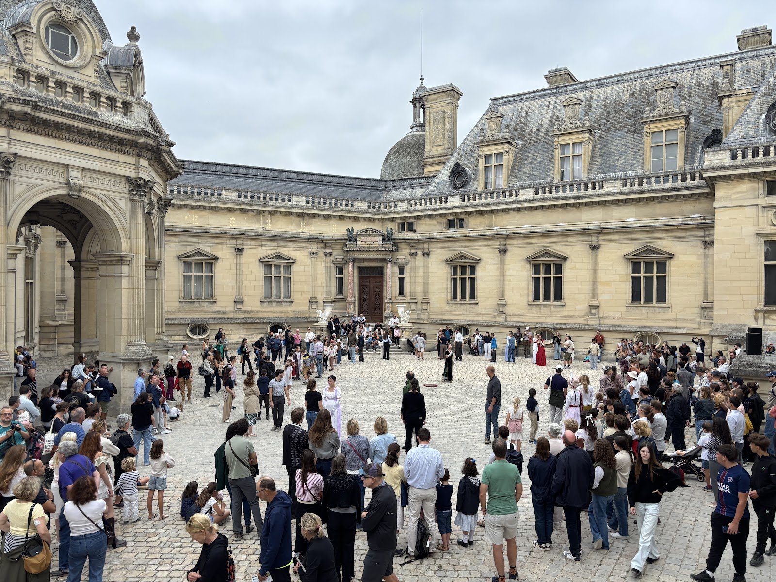 Grande ronde de participants dans la cour du château de Chantilly, entourée de spectateurs